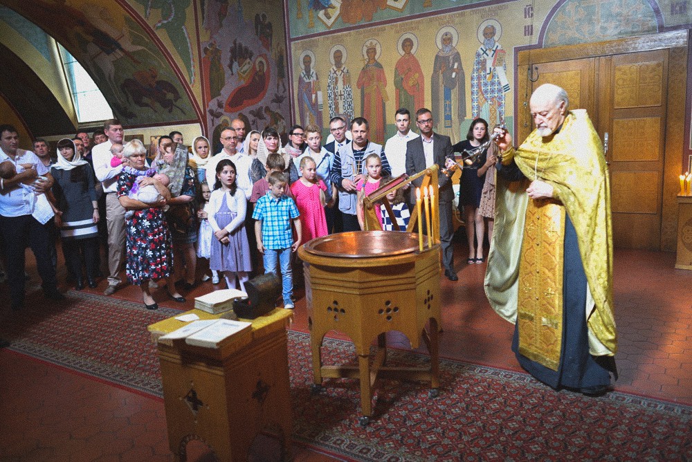 Priester steht mit der Gemeinde am Taufbecken während der Taufzeremonie