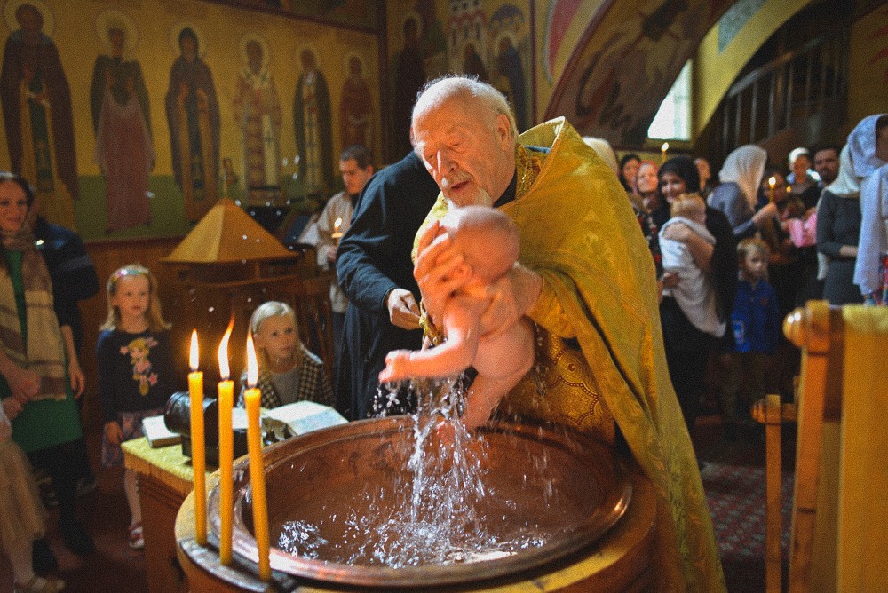 Priester tauft ein Baby im Taufbecken während einer orthodoxen Zeremonie