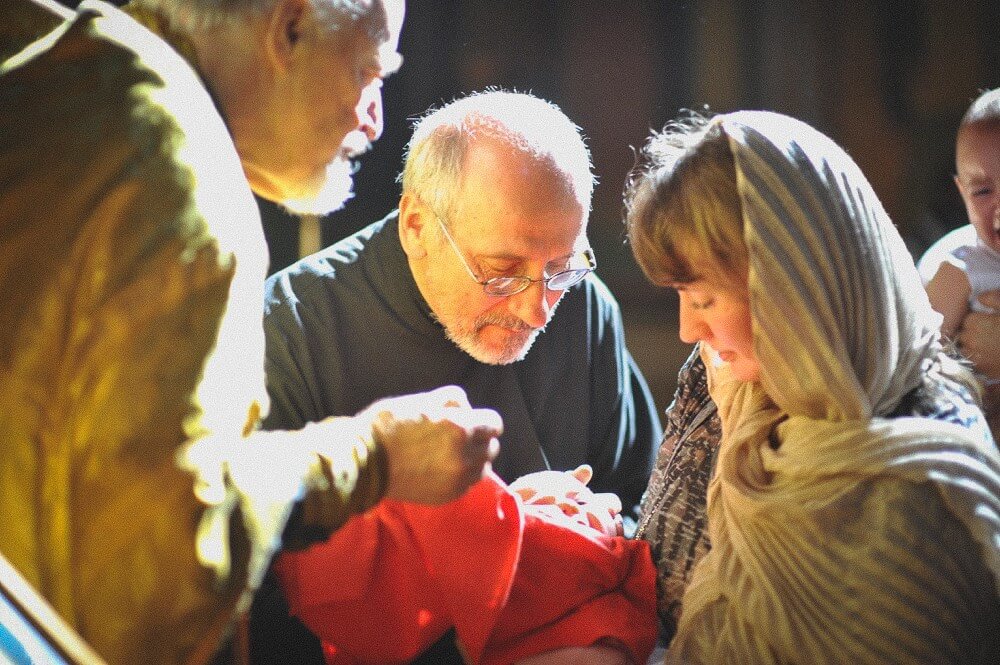 Eltern und Priester beugen sich während der Zeremonie über das eingewickelte Baby