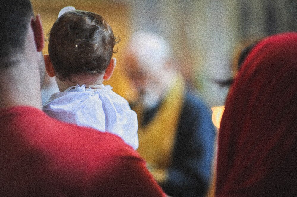 Baby im weißen Taufgewand wird während der Zeremonie auf dem Arm getragen