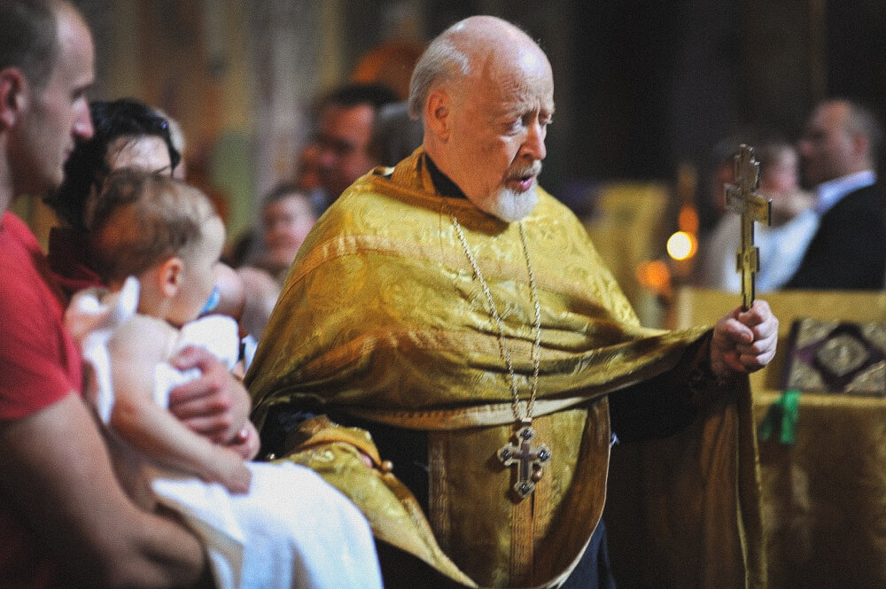 Priester hält ein Kreuz und segnet das Kind während der Taufe