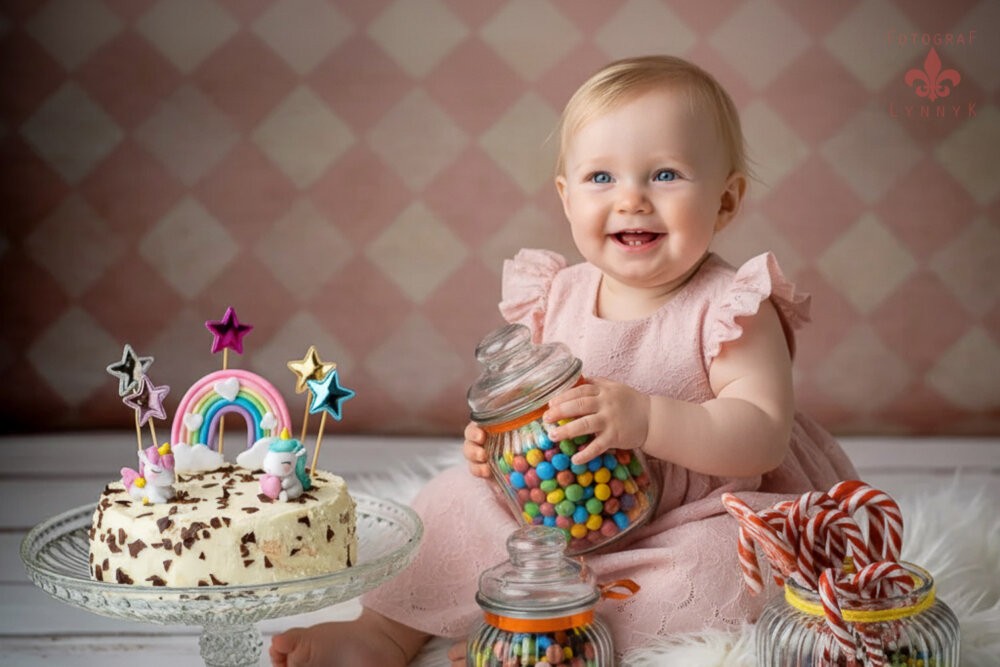 Lachendes Baby sitzt vor der Geburtstagstorte bei einem fröhlichen Cake-Smash-Shooting