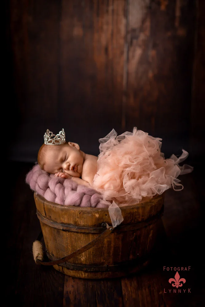 Baby in Körbchen mit rosa Federn – märchenhaftes Neugeborenenshooting.