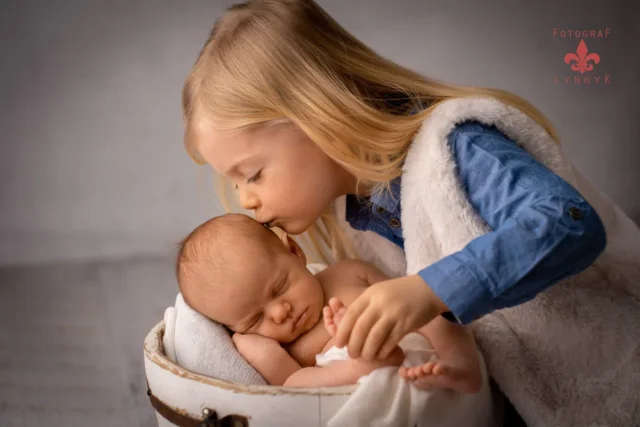 Geschwisterkind küsst ein Neugeborenes beim Familienfotoshooting